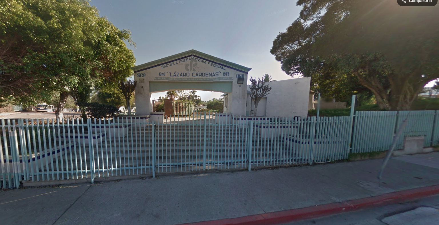 En la fotografía se muestra la entrada del plantel conformada por un arco color blanco y unas escaleras anchas. Sobre el arco, en letras grandes dice ESCUELA PREPARATORIA FEDERAL LÁZARO CÁRDENAS. Enfrente hay una reja azul que rodea la escuela.
